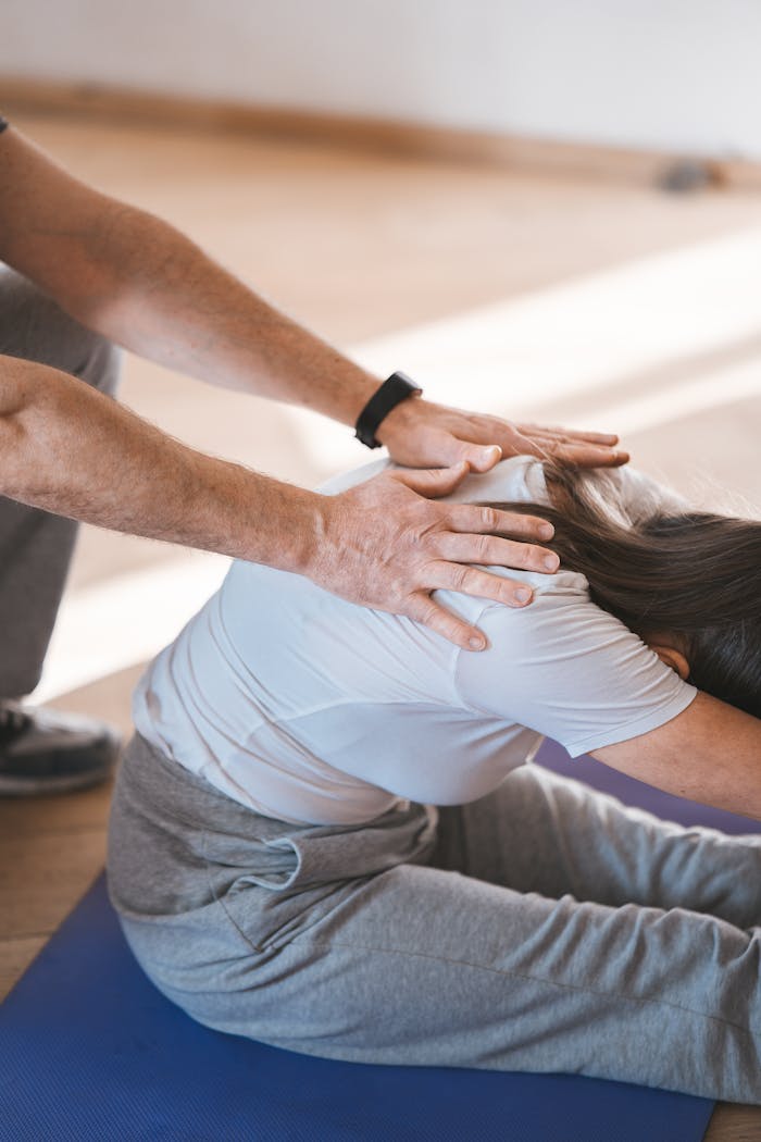 heros-img Person stretching on a yoga mat with assistance indoors. Exercise and wellness concept.